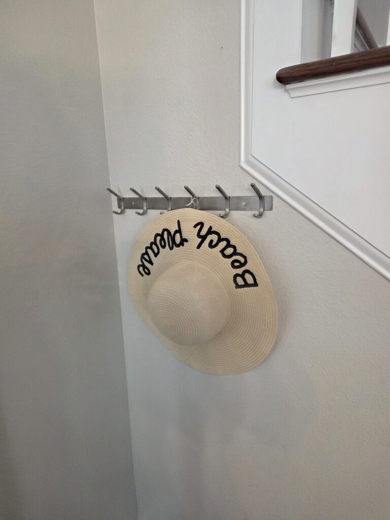 A straw sun hat reading Beach Please hanging on a hook
