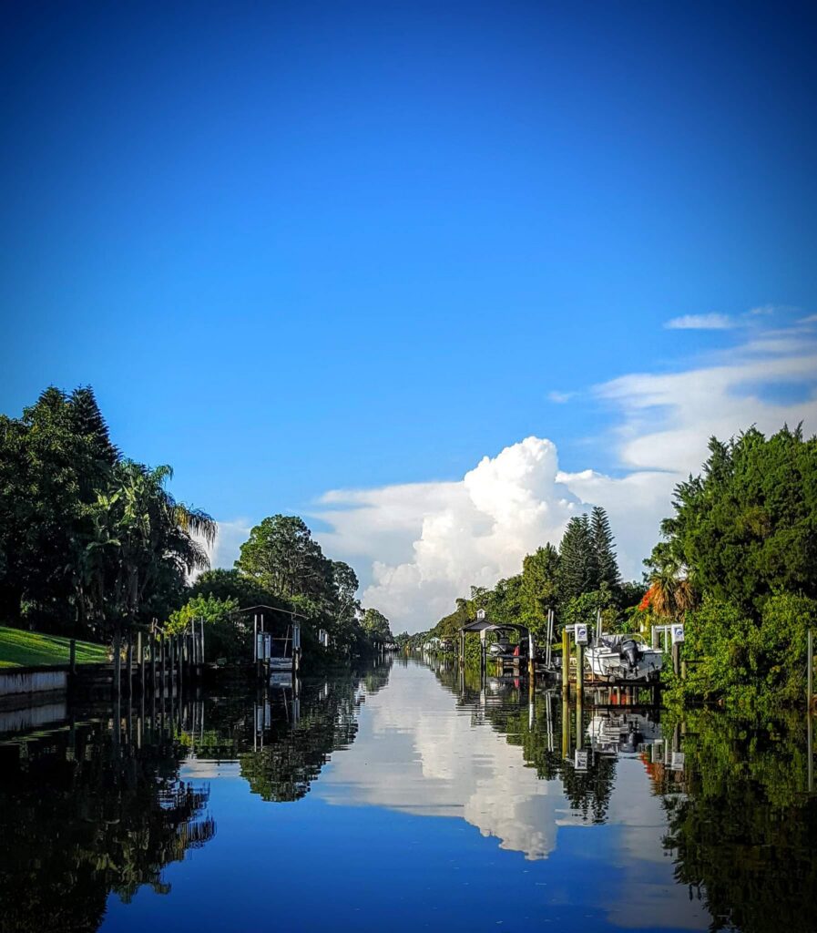 A quiet Bradenton canal lined with private docks and boat lifts, mirror calm under a blue Florida sky