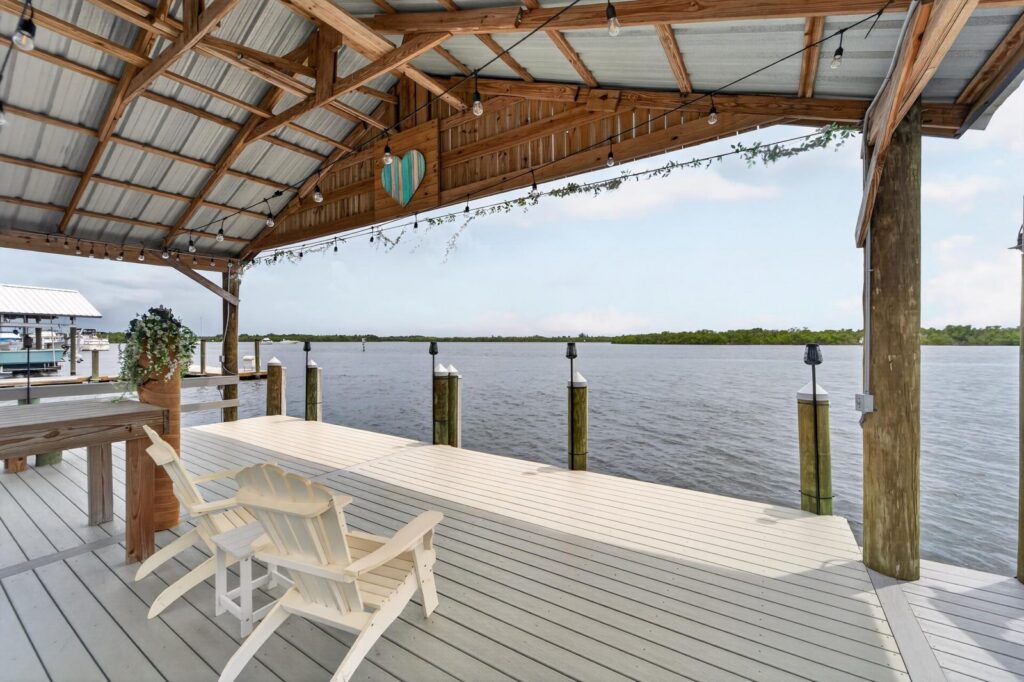 Covered private boat dock with Adirondack chairs looking out over open water and a mangrove shoreline in Florida