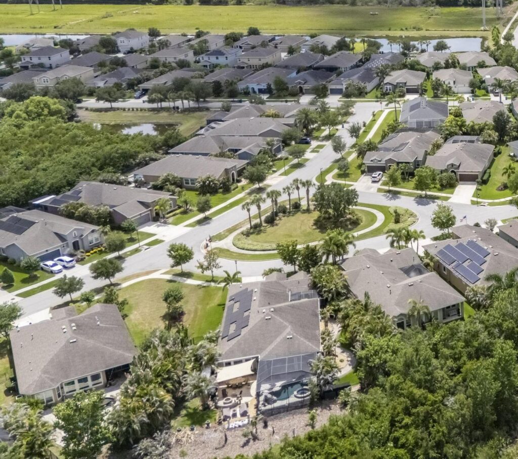 Aerial view of a Florida neighborhood of single-family homes with ponds, a landscaped roundabout and a wooded nature preserve behind the homes