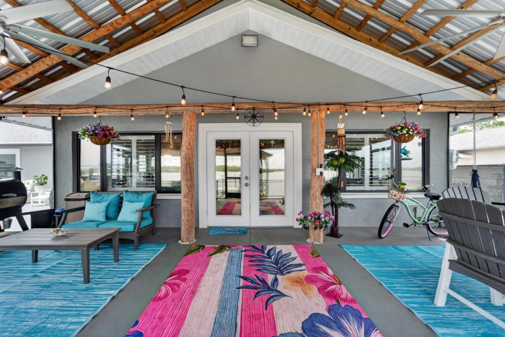 Covered back lanai with string lights and outdoor seating on a Florida waterfront home, with the water visible through the windows